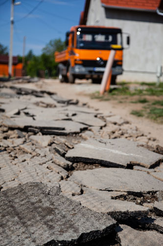 broken pieces of road in need of repair with an orange truck in the background