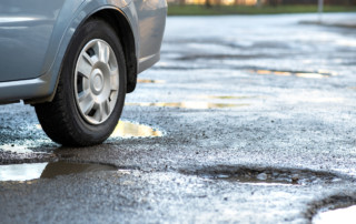 Close up of car wheel on a road in very bad condition with big potholes full of dirty rain water pools.