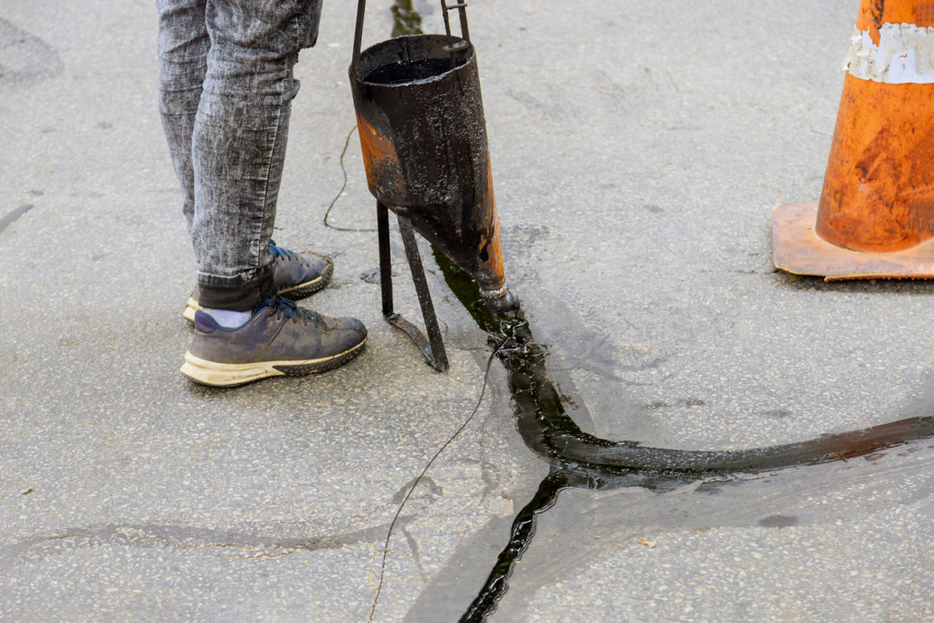 Man sealing asphalt driveway, sealcoating with filled cracks selective focus