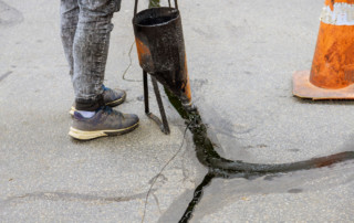Man sealing asphalt driveway, sealcoating with filled cracks selective focus