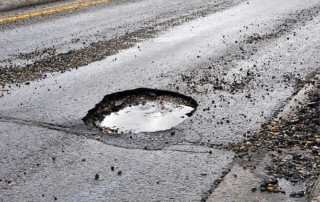 A large pothole in a road that has been damaged by rain, snow, and ice that is in need of repair.