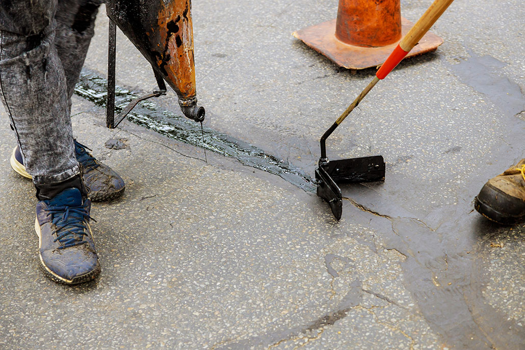 Road surface restoration work in the worker performs road patcher work repair of cracks by filling and sealing with coated by bitumen emulsion asphalt surface
