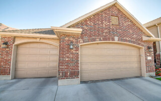 Detached double garage exterior with bricks and concrete driveway. There are two cream colored sectional garage doors complementing the red bricks wall.