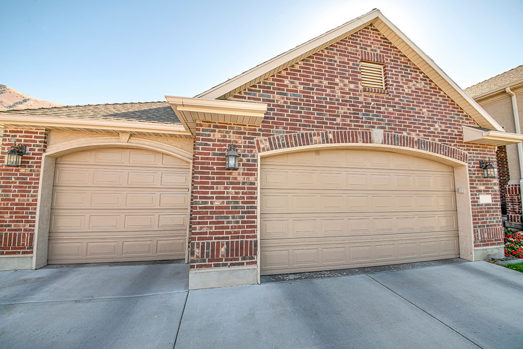 Detached double garage exterior with bricks and concrete driveway. There are two cream colored sectional garage doors complementing the red bricks wall.