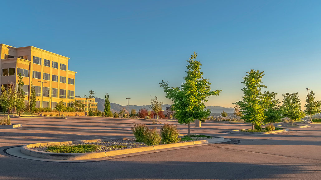 Panorama of a contemporary office building with parking lot on a sunny day. Mountain and sky is in the background of the commercial building.